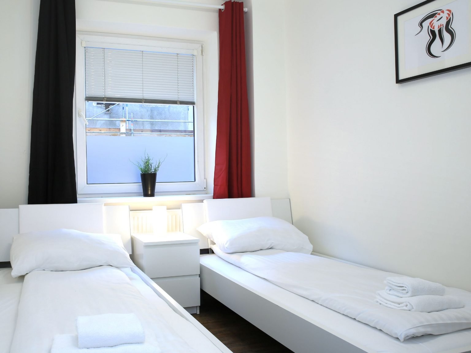 Zimmer mit zwei Einzelbetten und roten Vorhängen
