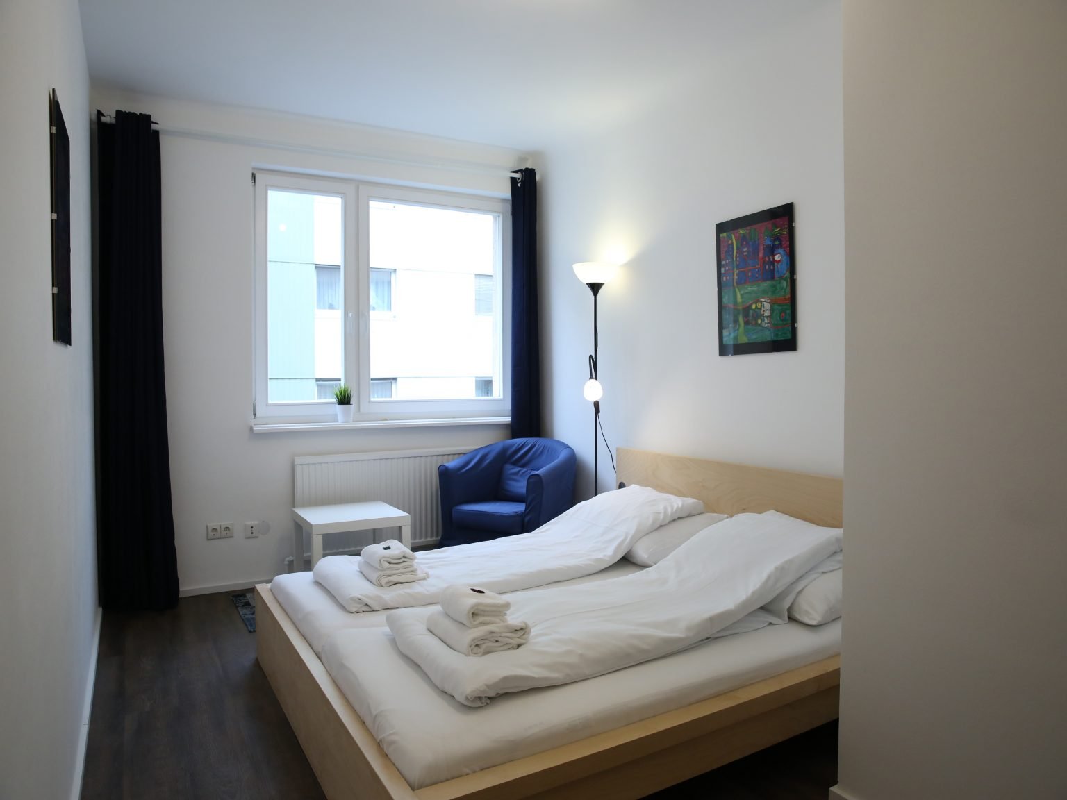 Modernes Schlafzimmer mit blauem Stuhl und hoher Lampe