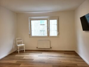 Raum mit weißem Stuhl, Heizkörper und einem Fernseher an der Wand
