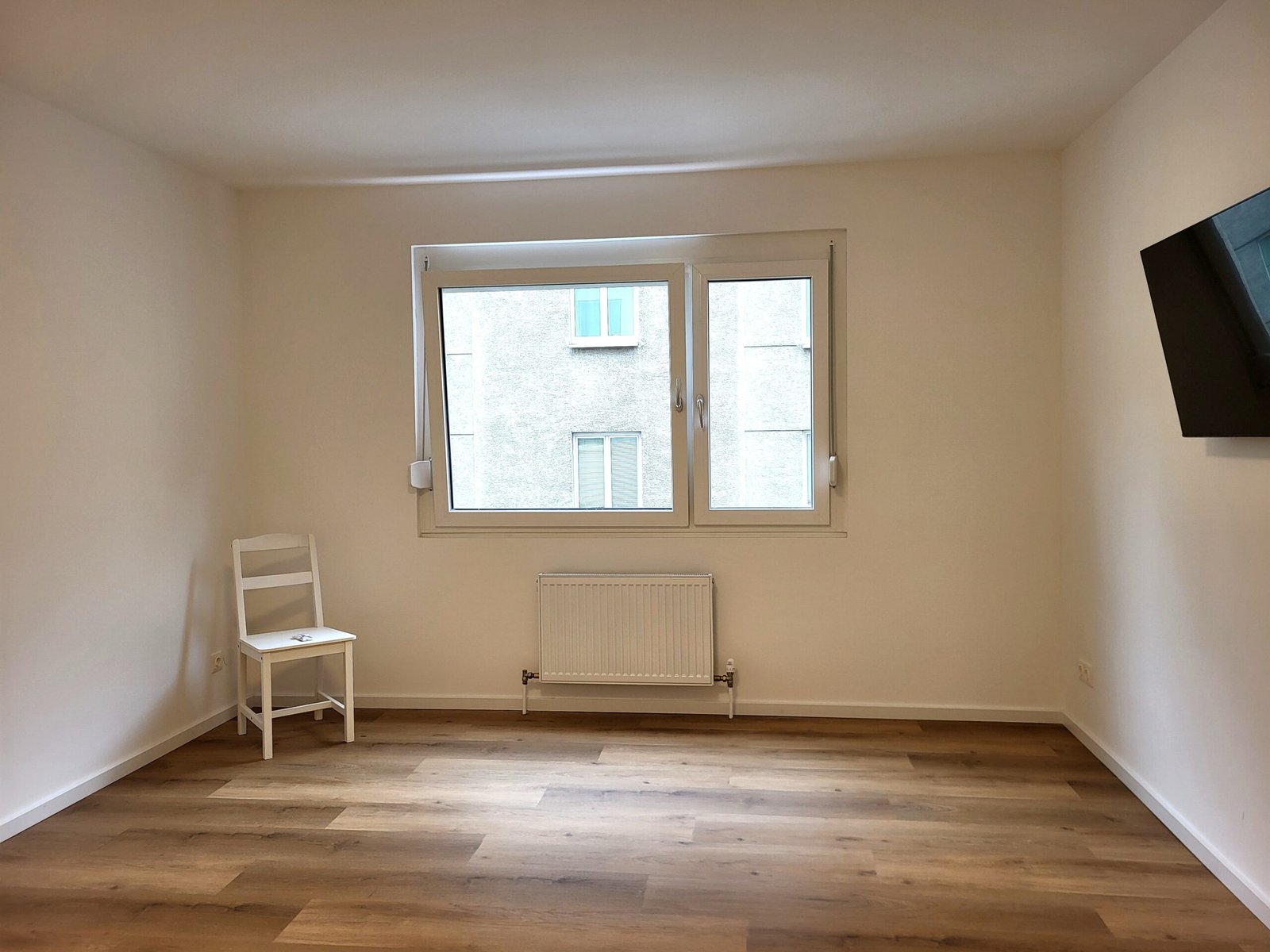 Raum mit weißem Stuhl, Heizkörper und einem Fernseher an der Wand